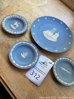 Four Wedgwood blue jasperware plates on a wooden surface: 8 inch Boston Tea Party plate, 5 inch Mayflower, 5 inch 1873-1973 plate, 4.5 inch jaguar plate.