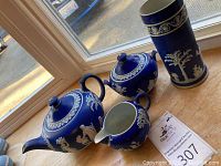 Group photo showing teapot, sugar bowl, creamer, and vase on window ledge with natural light. Highlights white jasperware relief on cobalt blue background.
