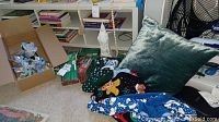 Wide shot showing a pile of Christmas-themed clothing including sweaters and fleece pants, green velvet pillow, and boxes with lights.