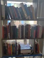 Books on shelves in a well-lit room, showing a diverse collection of hardback and paperback books in various sizes and colors.