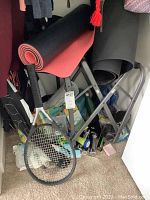 View showing two yoga mats rolled and resting on a black folding chair, tennis racket leaning against chair.