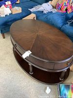Oval solid wood coffee table with polished dark brown finish, showing the smooth starburst patterned tabletop and drawer handles.