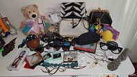 Overview of lot including teddy bear, handbags, glasses, costume jewelry, decorative mask, and small boxes with accessories.