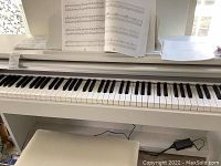 Front view of white digital piano showing full 88-key keyboard, sheet music on music rest and bench underneath