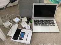 Overview of all items laid on carpet, including laptop, phone, cables, adapters, drives