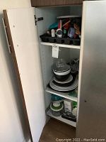 Kitchen cabinet showing shelves filled with stacked bowls, plates, storage containers, and some kitchen items.