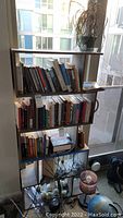Full view of tall asymmetrical wooden shelf filled with books, showing multiple staggered shelves and dark wood finish.