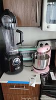 Photo showing full view of black Dash blender with clear pitcher, Dash toaster oven in mint green, and pink stand mixer.