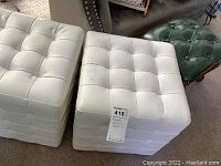 Two white square block stools with tufted upholstery placed side by side showing wear, alongside a smaller green tufted foot stool with wooden legs.