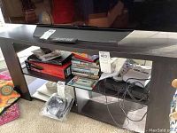 Full view of laminate TV stand with visible open shelving containing various items (not included in sale). The several shelves show books, games, and electronic cables stored beneath.