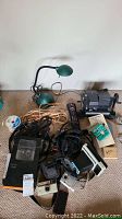 Photo shows Mansfield 8mm splicer, green desk lamp, Kodak CX7430 camera, Keystone 128 camera, various cords, remotes, and an iPhone among other items.