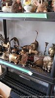 Wide view of brass decorative items including candle holders, animal figurines and containers arranged on shelves