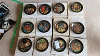 Twelve plates displayed on their original boxes showing assorted folkloric scenes