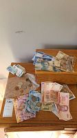 Overview of multiple foreign currency bills and coins arranged on wooden desk.