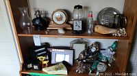 Wood shelf with assorted items including a wooden mantle clock, gum ball machine, figurines, photo frames, metal plates, shell, bottle and wooden carved item