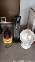Lot includes a yellow and red Stinger wet/dry vacuum, a tall black and silver Presto Heatdish heater, and a short white Bionaire heater standing on floor near door and white appliance.