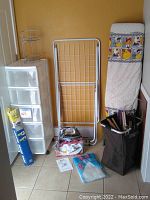 Photo showing the full lot including the plastic drawers, sweater dryer rack, ironing board with Looney Tunes cover, hamper, Shark iron on the floor with instruction manuals, and hangers.