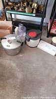 Photo showing Presto pressure cooker-canner, FoodSaver vacuum sealer, and Tefal Super Fryer placed on the ground with background furniture.