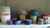 Wide view showing pastel bowls stacked on the left, various small bowls and mushroom-shaped canisters in the center, blue mushroom-shaped canister and brown one next to them.