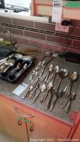 Wide view of silver plated flatware spread across countertop and tray showing variety of items.