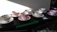 Seven tea cups and saucers displayed on a table under sunlight