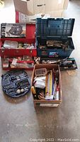 Overview of the lot showing the metal toolbox, plastic toolbox, cardboard box with tools, and the closed drill accessory case.