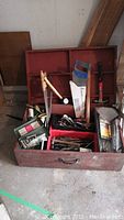 Wide shot of the open homemade wooden toolbox filled with assorted hand tools including hammer, mallet, saw, screwdriver, crowbar