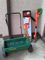 Photo showing the GreenThumb spreader and Black & Decker grass trimmer leaning against a wall with the trimmer box in the background.