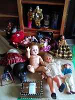 Overview photo showing various vintage dolls, figurines, baby shoes, and the music box on a floor.