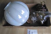 White scalloped glass globe lamp shade with brass top decorative fitting, resting inside a cardboard box.