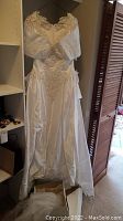 Full length photo of the white wedding dress hanging, showing lace applique and satin fabric details