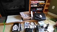 Full lot view showing Wii console with controllers, Wii Fit board, Wii racket, telephone, and miscellaneous electronics on floor by fireplace.