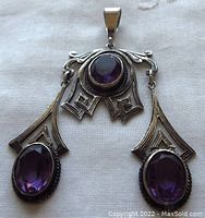 Front view of antique sterling silver pendant displaying three faceted purple stones and detailed openwork silver design.