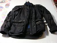 Full view of black Joe Rocket motorcycle jacket laid flat to show design, pockets, and adjustable straps.