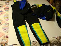 Photo showing the entire wet suit laid out flat on a surface, displaying the jacket and pants with black base and yellow and turquoise accents.