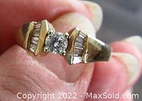 Close-up angled view of yellow gold ring showing center round diamond and baguette side stones