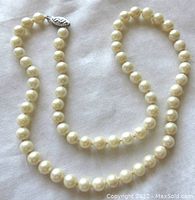 Full view of the vintage cultured pearl necklace laid out on fabric, showing round creamy white pearls and filigree clasp.