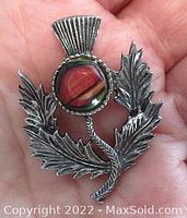 Front view of vintage Celtic Scottish thistle brooch held in hand showing pewter finish and central reddish glass stone.