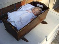 Wooden crib with doll inside showing length and width, crib on table outside