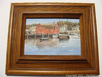 Framed oil painting showing a red building and boats at a harbor, dockside scene in a wooden oak frame.