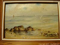 Frontal view of the vintage seascape oil painting showing rocks, water, birds, and sailboats with frame.
