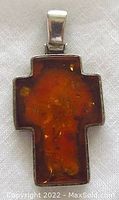 Front view of vintage amber cross pendant set in sterling silver, showing warm orange-brown amber with inclusions visible inside.