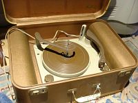 Opened brown suitcase style record player showing the turntable, tonearm, and speed control knob.