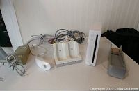 Wii console with accessories on table, including power adapter, sensor bar, charger dock, and AV cables.