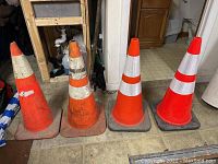 Four orange traffic cones in an indoor setting on a tiled floor showing condition differences.