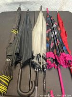 Five umbrellas in various colors and handle styles arranged side by side.