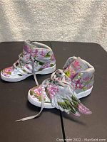 Pair of Adidas Jeremy Scott Wings high top sneakers, white with floral pink and green pattern and wing attachments.