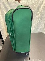 Green rolling suitcase exterior profile showing fabric, wheels and handle.