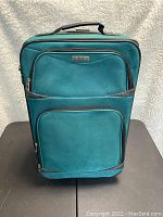 Front view of teal carry on bag showing two front zipper pockets and brand label