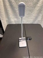 LED desk lamp with flexible neck, rectangular lamp head, and USB charging base with power adapter on black surface.